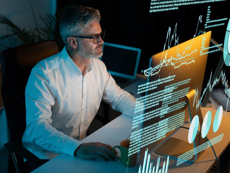 man on computer at night with charts and data overlaid